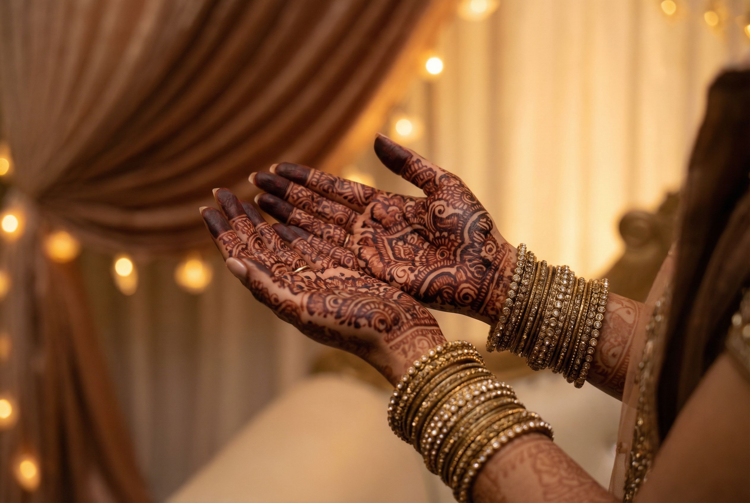 Bride's hands showing elaborate traditional bridal mehndi henna designs with golden bangles