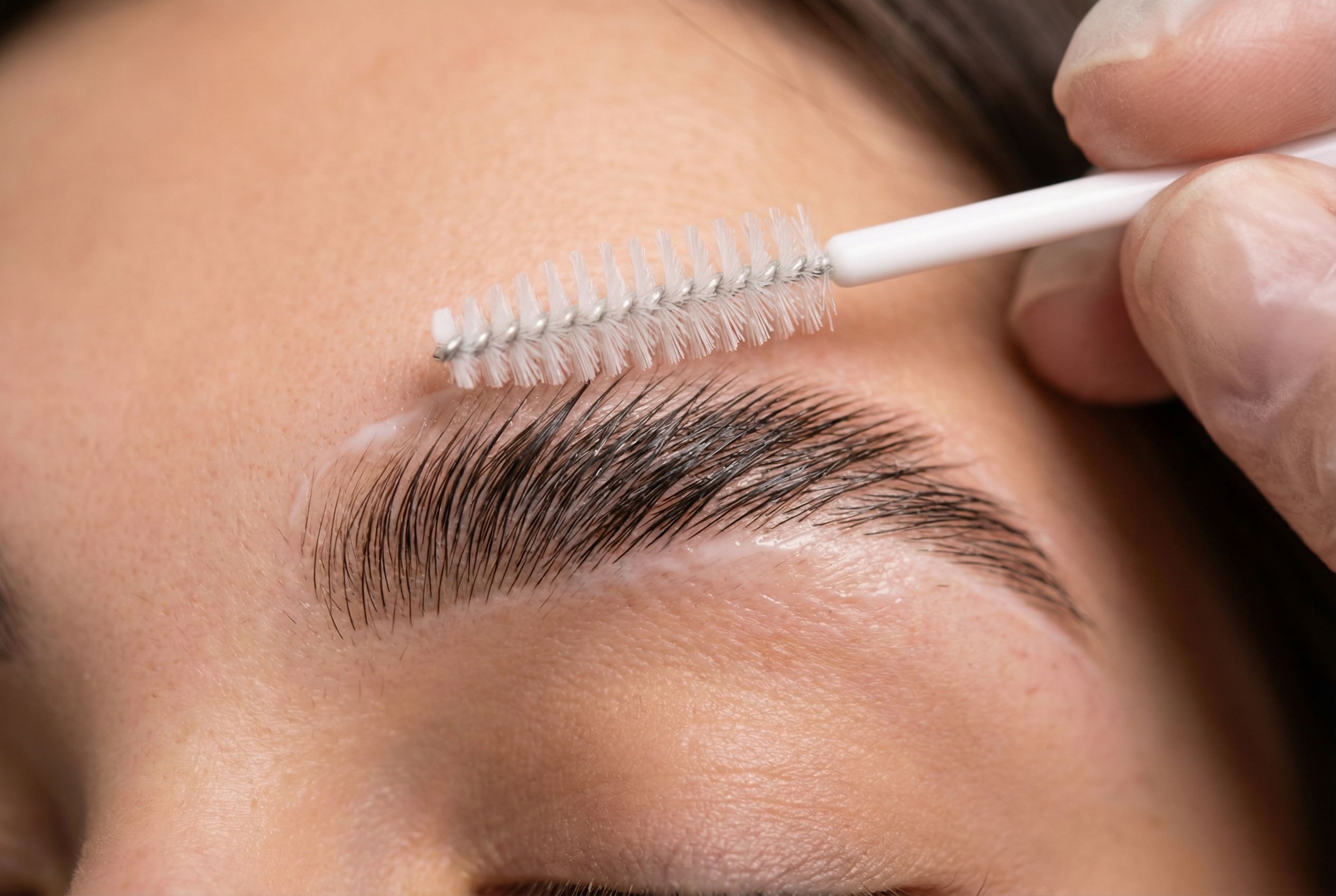 Brow artist brushing eyebrow hairs upward during the lamination shaping step